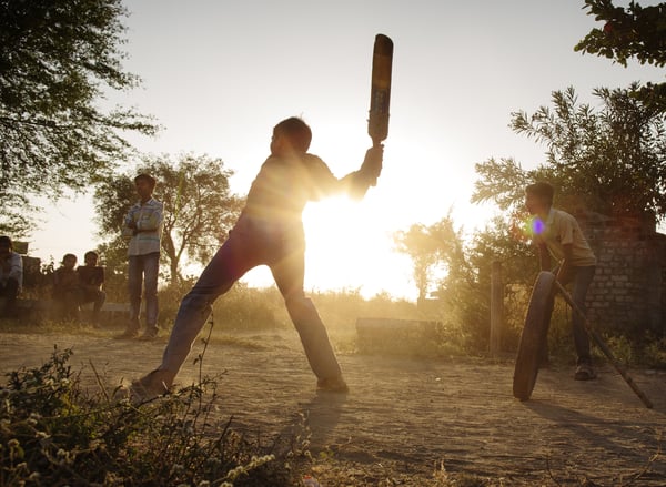 Plusieurs adolescents jouant au cricket au coucher du soleil.