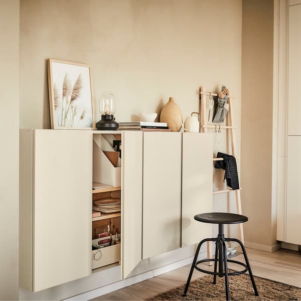 Plusieurs armoires IKEA IVAR en bois sur un mur avec des accessoires décoratifs sur le dessus et un tabouret noir au premier plan.