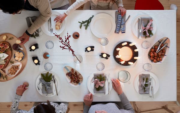 Plusieurs personnes assises autour d’une table décorée pour une occasion festive: serviettes, décorations, bougies LED allumées, plateau de fromages.