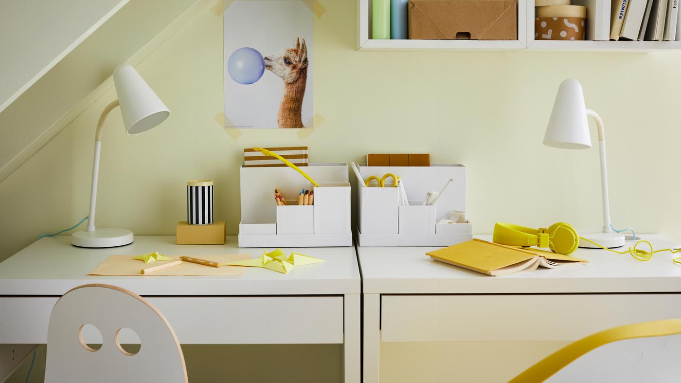 Pod schodiskom stoja dva stoly MICKE s lampami FUBBLA. Pri jednom stole sa nachádza detská stolička k písaciemu stolu, pri druhom otočná stolička.