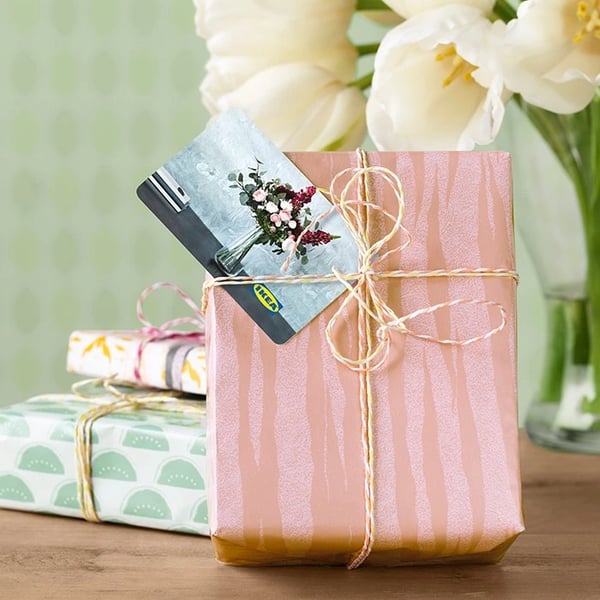 Подарочная упаковка из светло-розовой бумаги с подарочной карточкой под лентой.