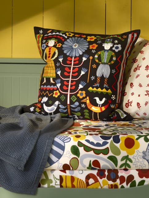 Poduszki dekoracyjne i pled leżące na łóżku ze wzorzystym prześcieradłem.