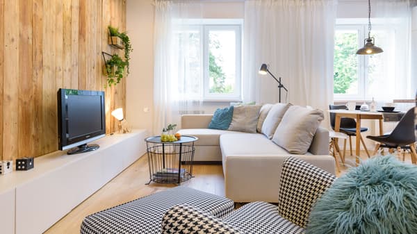 Pokój dzienny z drewnianą ścianą, na tle kórej stoi szafka BESTÅ z telewizorem. Przy szafce stoi beżowa sofa i metalowy stolik kawowy.