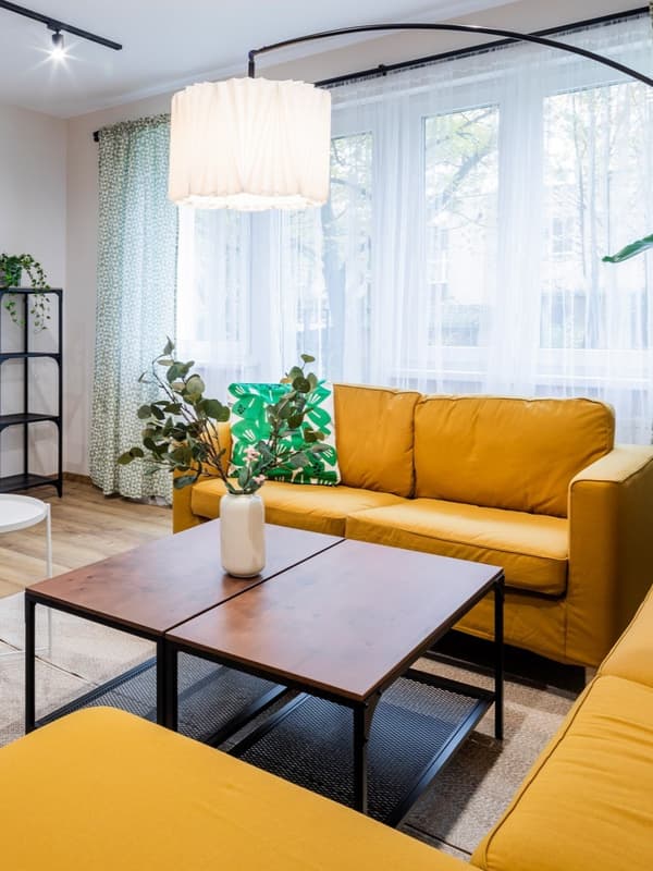 Pokój dzienny z trzema zółtymi sofami i brązowym stoliczkiem kawowym pośrodku
