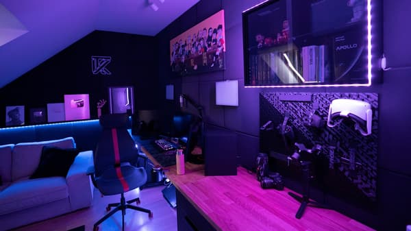 Pokój gamingowy z czarnymi ścianami i meblami z asortymentu gaminowego z różowym oświetleniem.