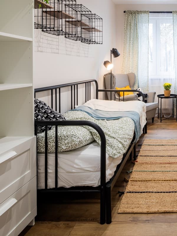Pokój młodzieżowy z pojedynczym łóżkiem o czarnej, metalowej ramie. Na dwynie chodniczek w naturalnych kolorach 