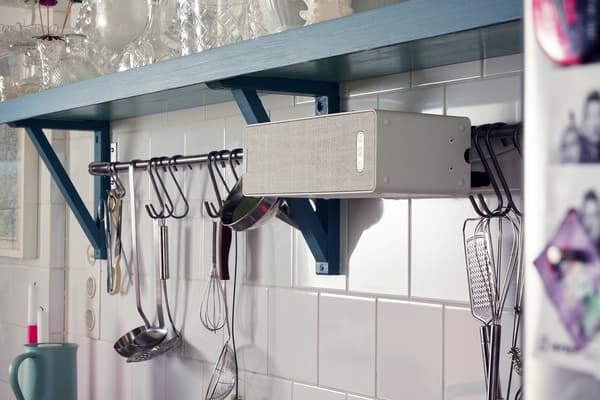 Polica SYMFONISK so zabudovaným reproduktorom na stene v kuchyni vedľa zaveseného kuchynského náčinia.