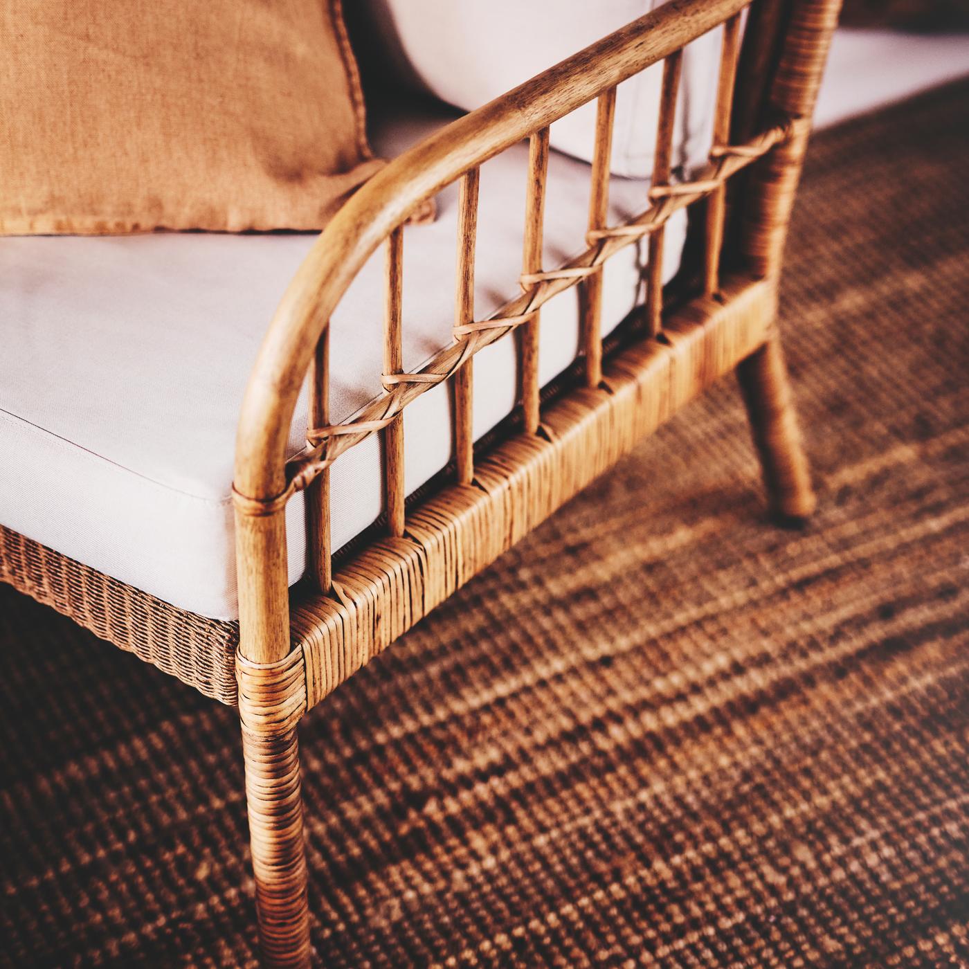 Poltrona HOLMSTA/FRÖKNABO in legno e rattan con cuscini sedile/schienale bianchi e cuscino marrone, su un tappeto a tessitura piatta LOHALS.