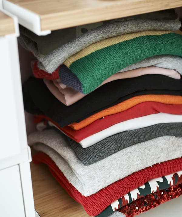 Pormenor de uma pilha de roupa de malha colorida, dobrada em cima de uma prateleira.