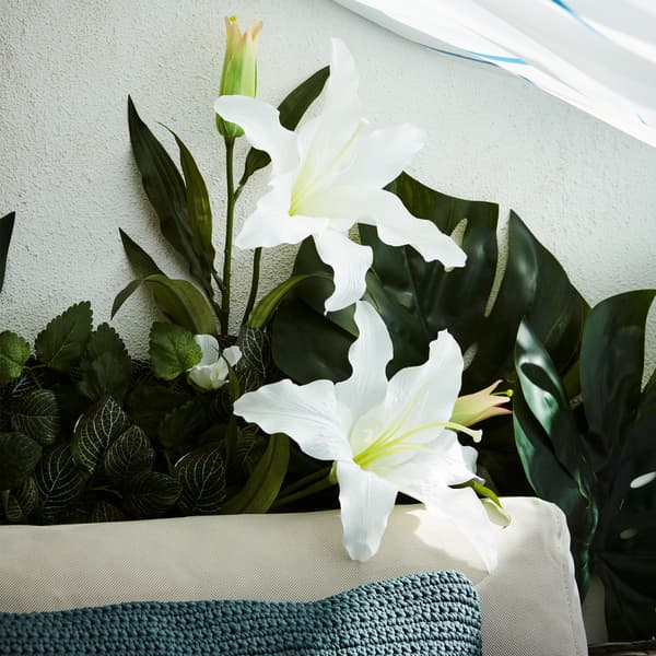 Pormenor do sofá com vegetação artificial que cobre a maior parte da parede da varanda, à sombra de uma cortina de duche.