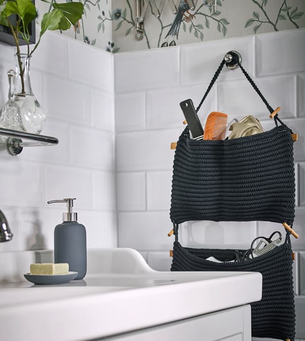 Portaoggetti da appendere NORDRANA blu pieno di prodotti per il bagno, appeso alle piastrelle bianche di un bagno - IKEA.