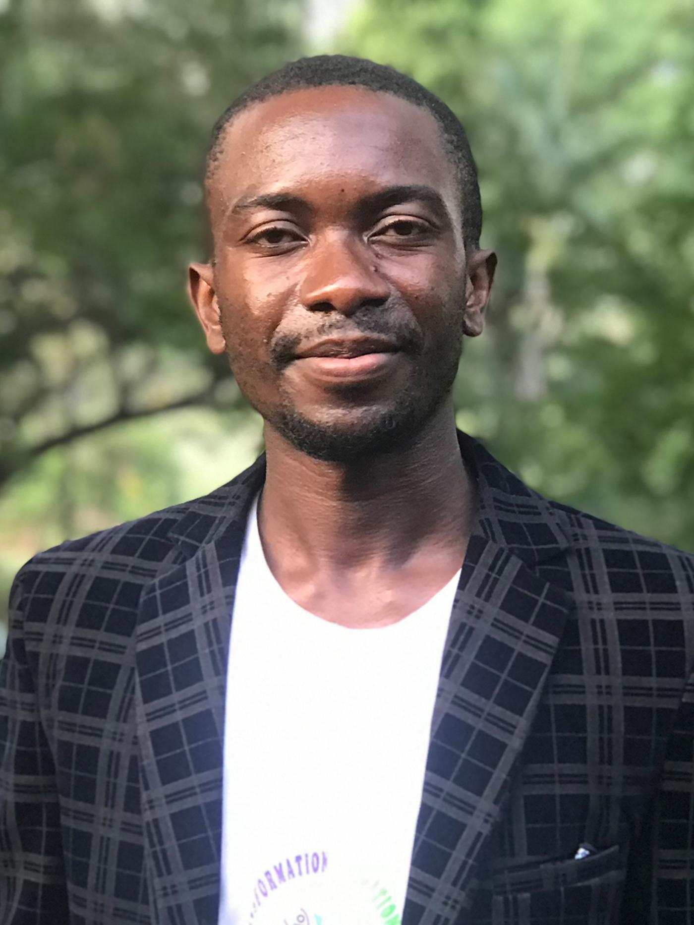 Portrait of Barthelemy, a Congolese reufgee, smiling at the camera wearing a dark blazer and white shirt.