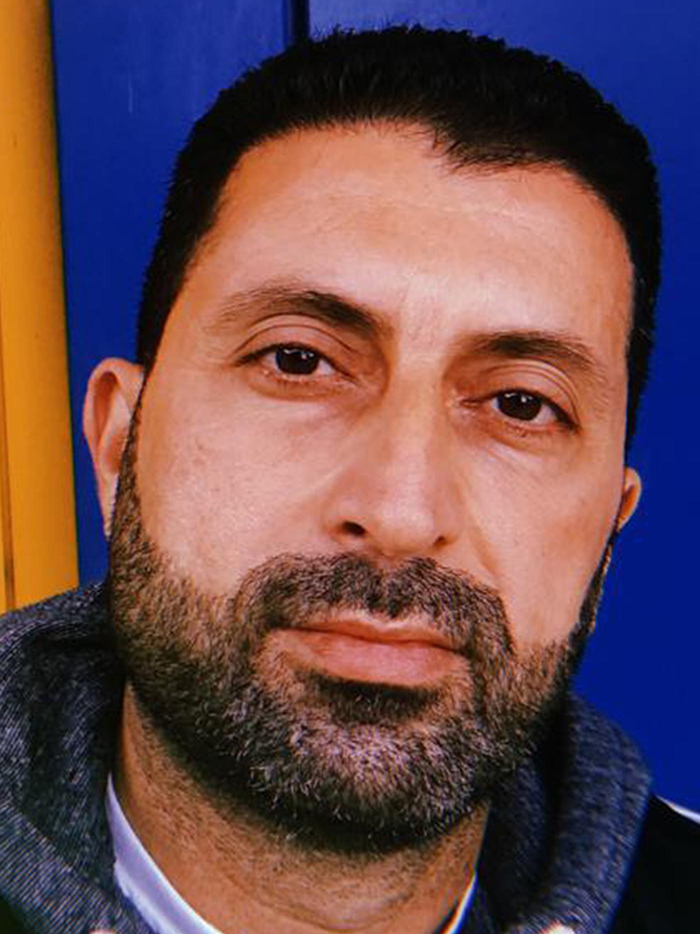 Portrait of Odai, an Iraqi refugee and IKEA Switzerland co-worker, staring straight at the camera against a blue background.