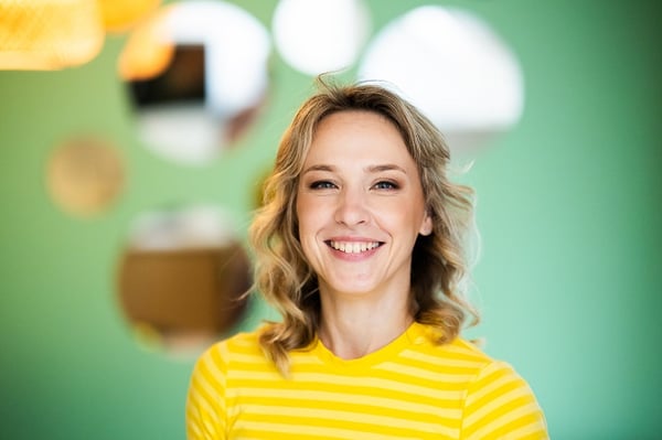 Portrait of smiling woman in yellow striped shirt against green accent wall
