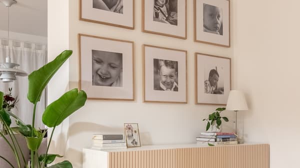 Portrety dzieci w brzozowych ramkach wiszące na ścianie nad szafką w pokoju dziennym.
