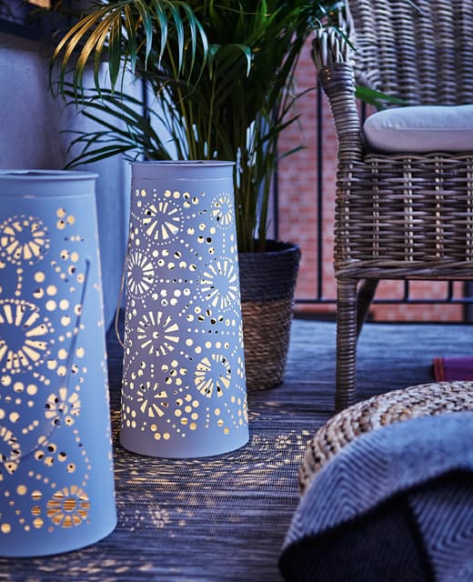 Posées au sol, deux lanternes solaires à DEL en métal blanc illuminent le balcon une fois le soir venu.