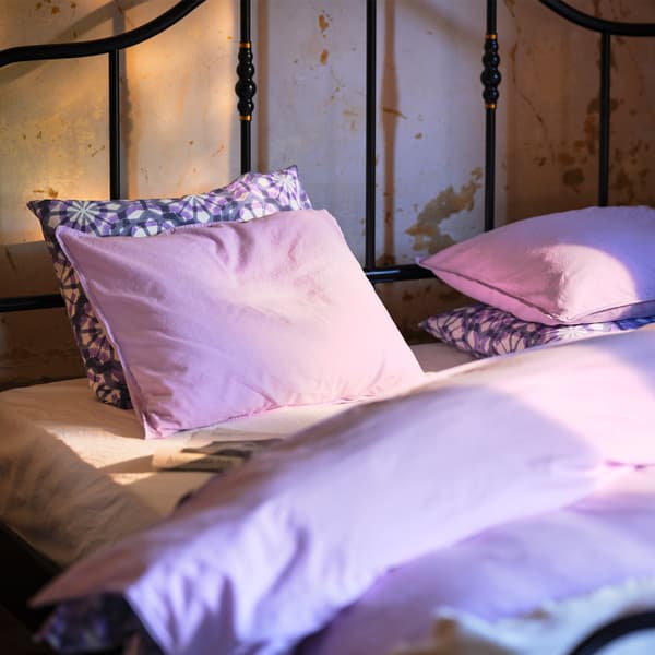 Posteľ s čiernym oceľovým rámom pri vidieckej béžovej stene s detailmi v mosadznej farbe.