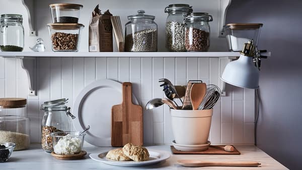 Pots de vidre, plats i estris de cuina d'IKEA en una taula i un prestatge blanc.