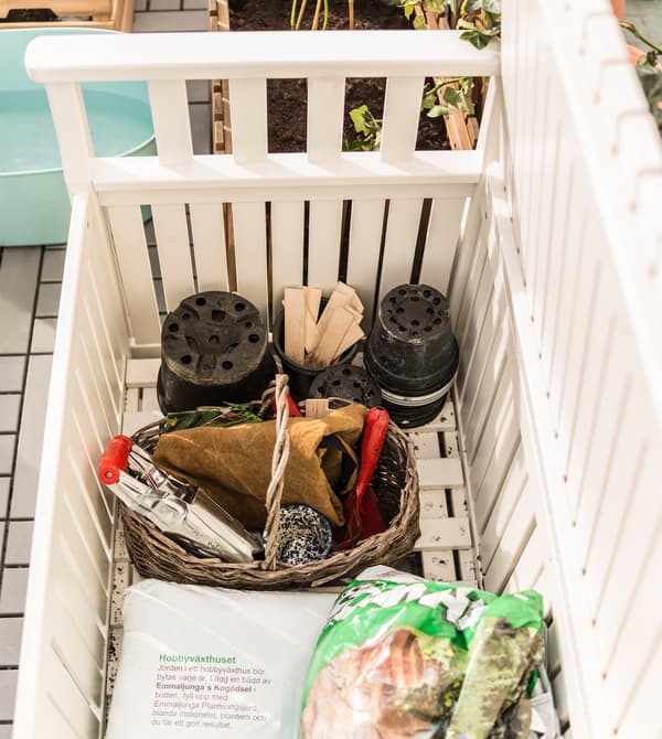 Pots, outils et terreau rangés dans un banc de rangement blanc.