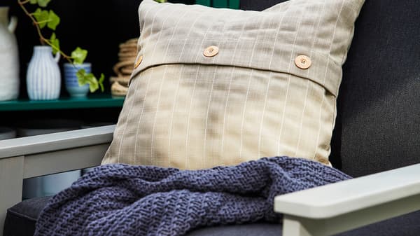 Povlak na vankúš FESTHOLMEN, ktorý je vhodný pre vonkajšie použitie, je položený na vonkajšej sedačke.