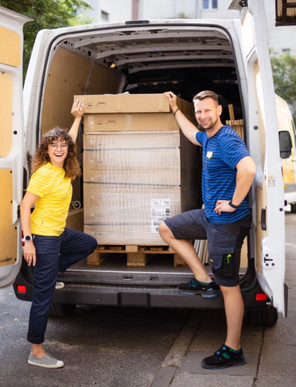 Pracownica i Pracownik IKEA pozujący na tle otwarte samochodu dostawczego z meblami na palecie. 