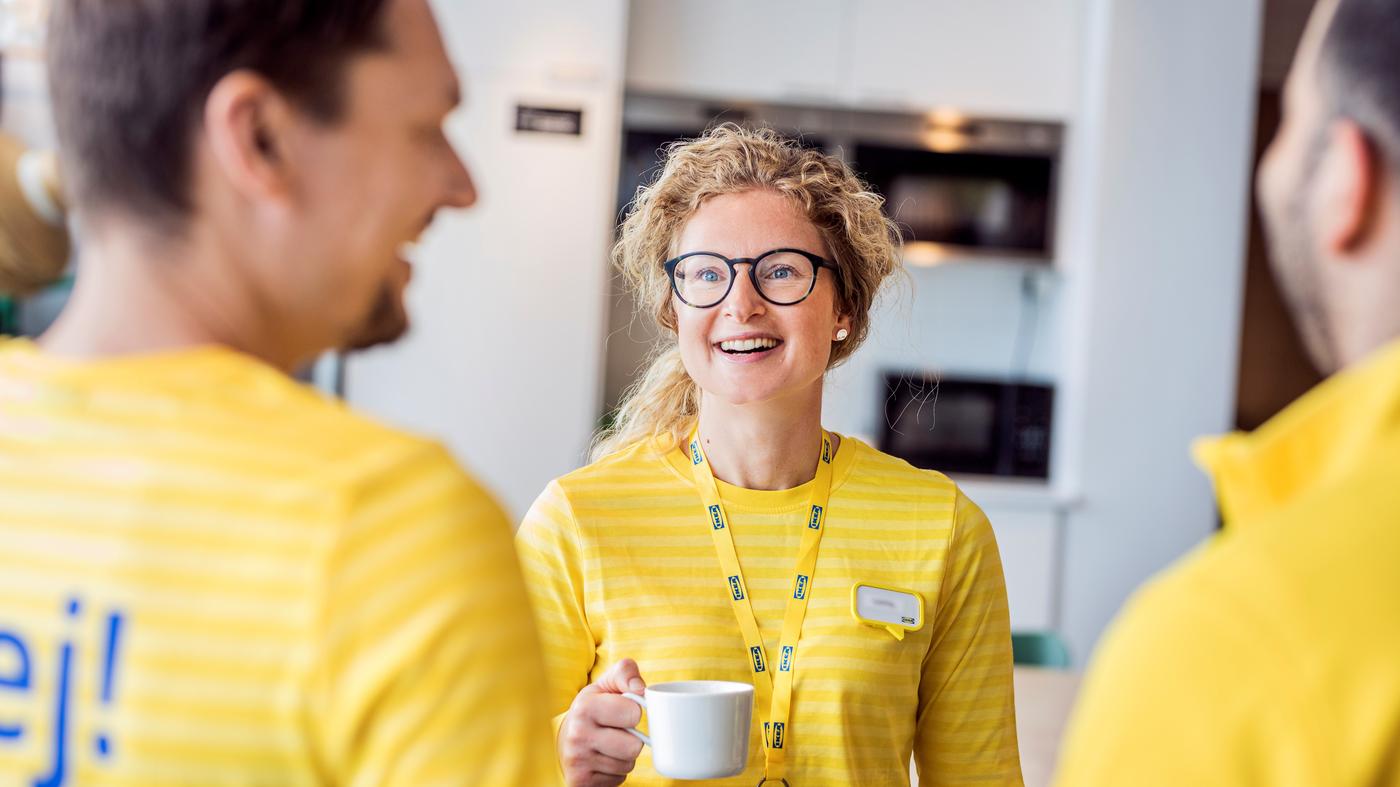 pracowniczka IKEA stoi z kubkiem i rozmawia z dwoma kolegami z pracy