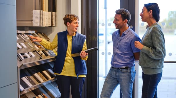 Pracowniczka sklepu IKEA rozmawia z kobietą i mężczyzną i prezentuje różne modele uchwytów i wykończenia mebli przy ekspozycji.