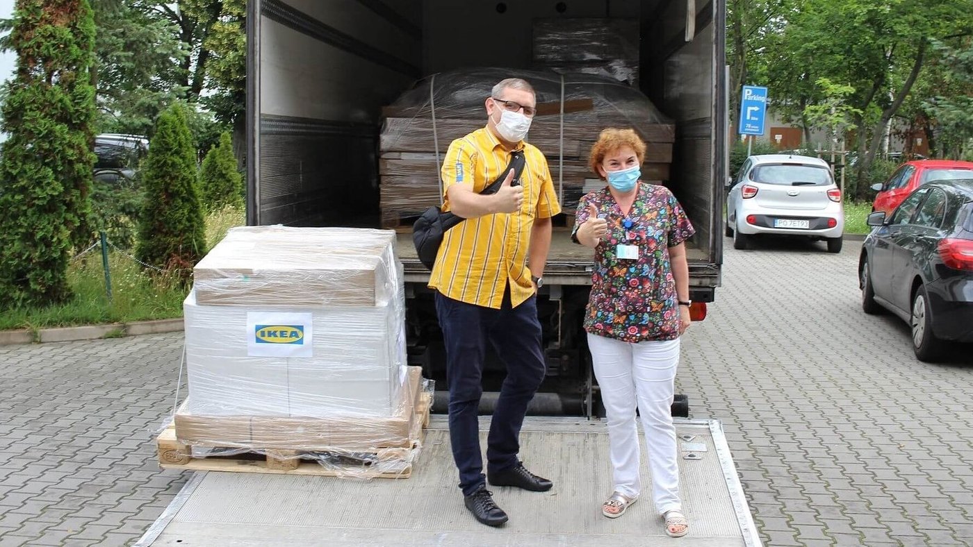 Pracownik IKEA i pracowniczka jednego z oddziałów psychiatrycznych stoją uśmiechnięci obok ciężarówki z produktami IKEA przeznaczonymi dla dzieci i młodzieży