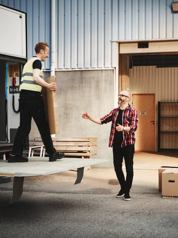 Pracownik IKEA stojący na platformie samochodu dostawczego skierowany w stronę klienta, który zamierza odebrać flatpack.