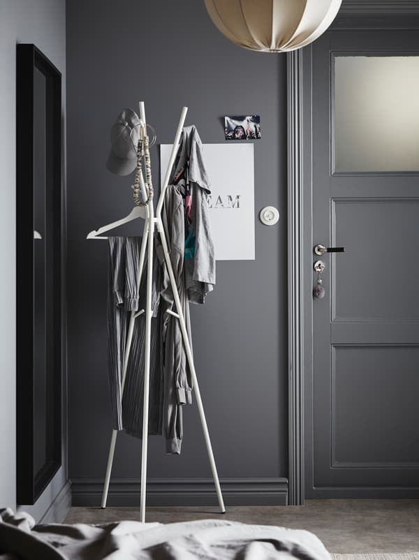 Predsieň natretá sivou farbou s bielou lampou a minimalistickým bielym vešiakom EKRAR s tromi nohami. 