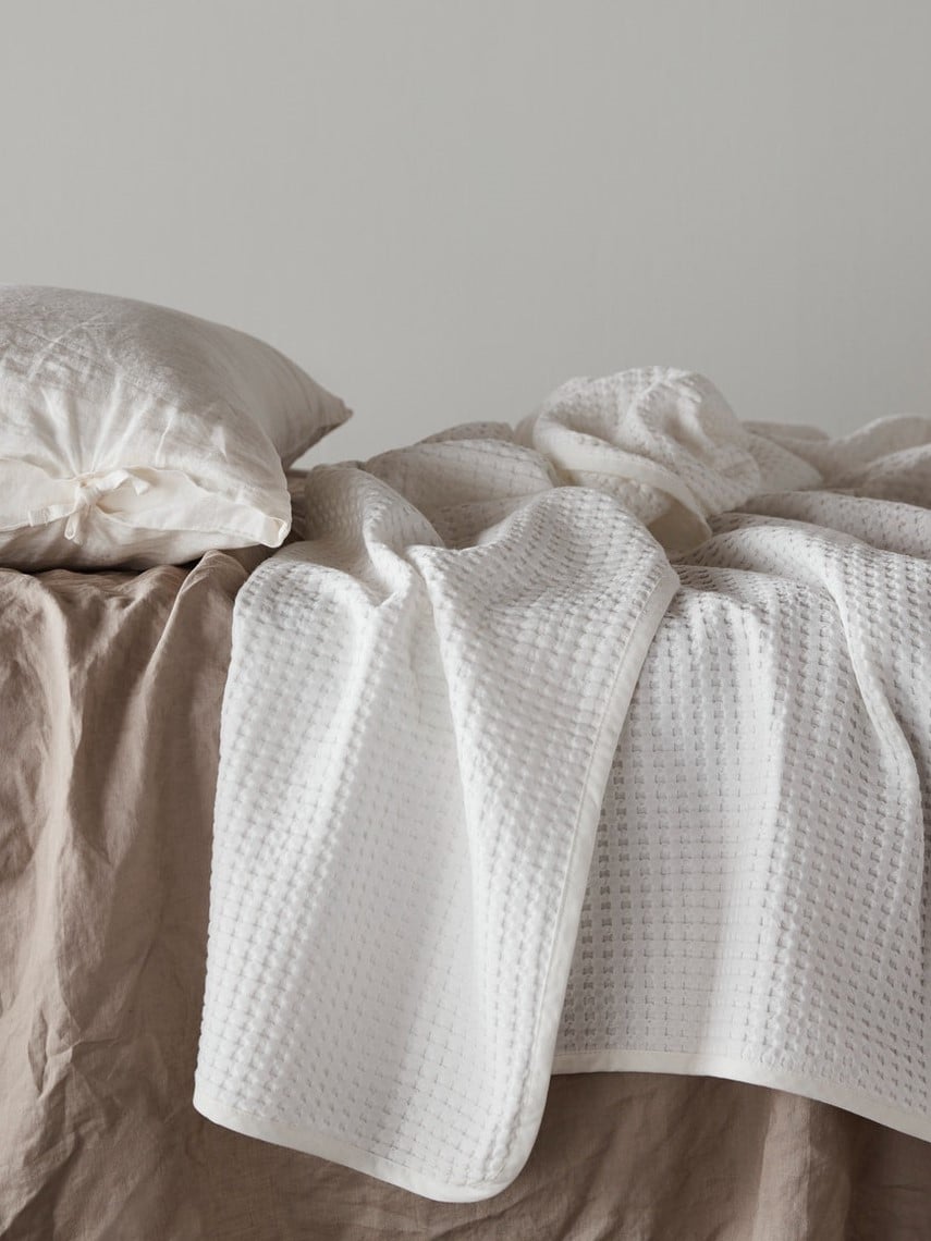 Přehozy na postel v bílé a hnědé barvě.