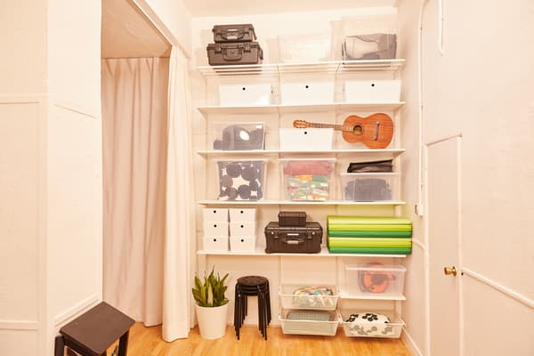 Prestatgeria modular amb objectes ordenats en caixes transparents i opaques. Tamborets apilats, una planta i una escala plegada.