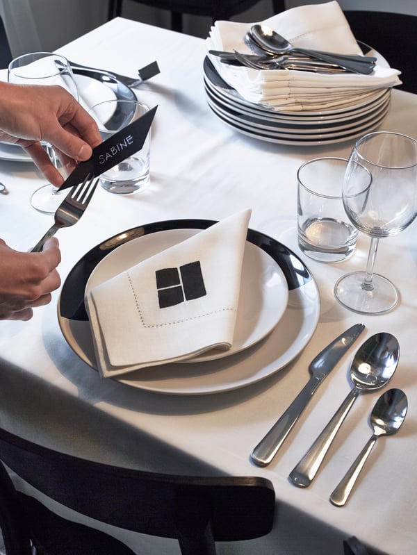 Příbory DRAGON na bílém ubruse vedle černobílého talíře TICKAR.