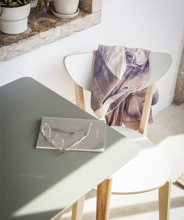 Prim plan cu o masă gri și un scaun alb scăldate în lumina soarelui.