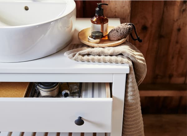 Primeiro plano do lavabo, unha toalla e xabóns sobre un toucador branco co caixón aberto.