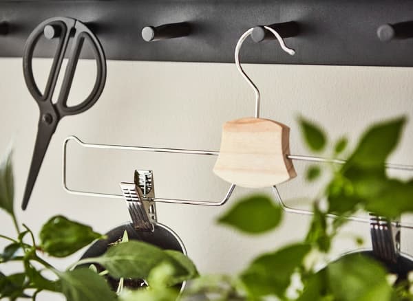 Primeiro plano dunha percha cromada IKEA BUMERANG para pantalóns/saias colgada nun colgadoiro de parede.