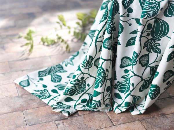 Primeiro plano dunhas cortinas ALPKLÖVER ata o chan cun deseño de follas de figueira en branco e verde.