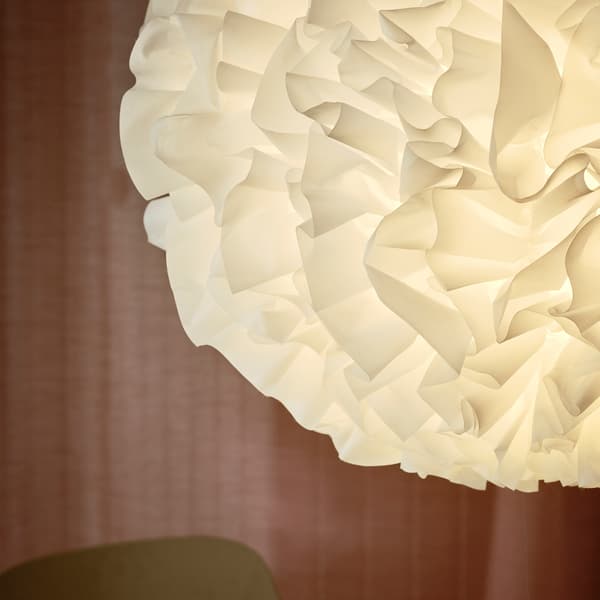 Primo piano della lampada a sospensione VINDKAST, realizzata con morbide increspature bianche a forma di pompon, e tenda rosa sullo sfondo.
