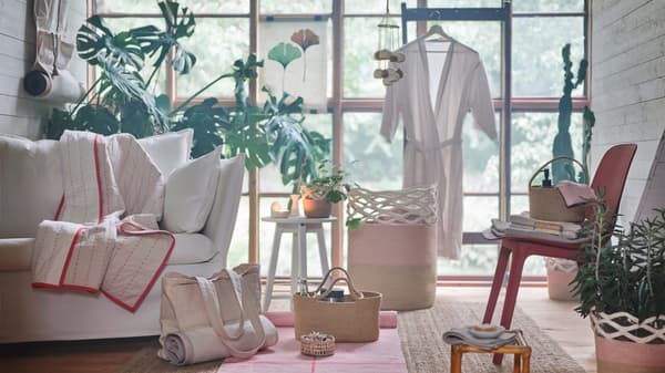 Products from the VÅRDANDE collection are arranged against a wooden framed window in a living room with plants and a sofa.