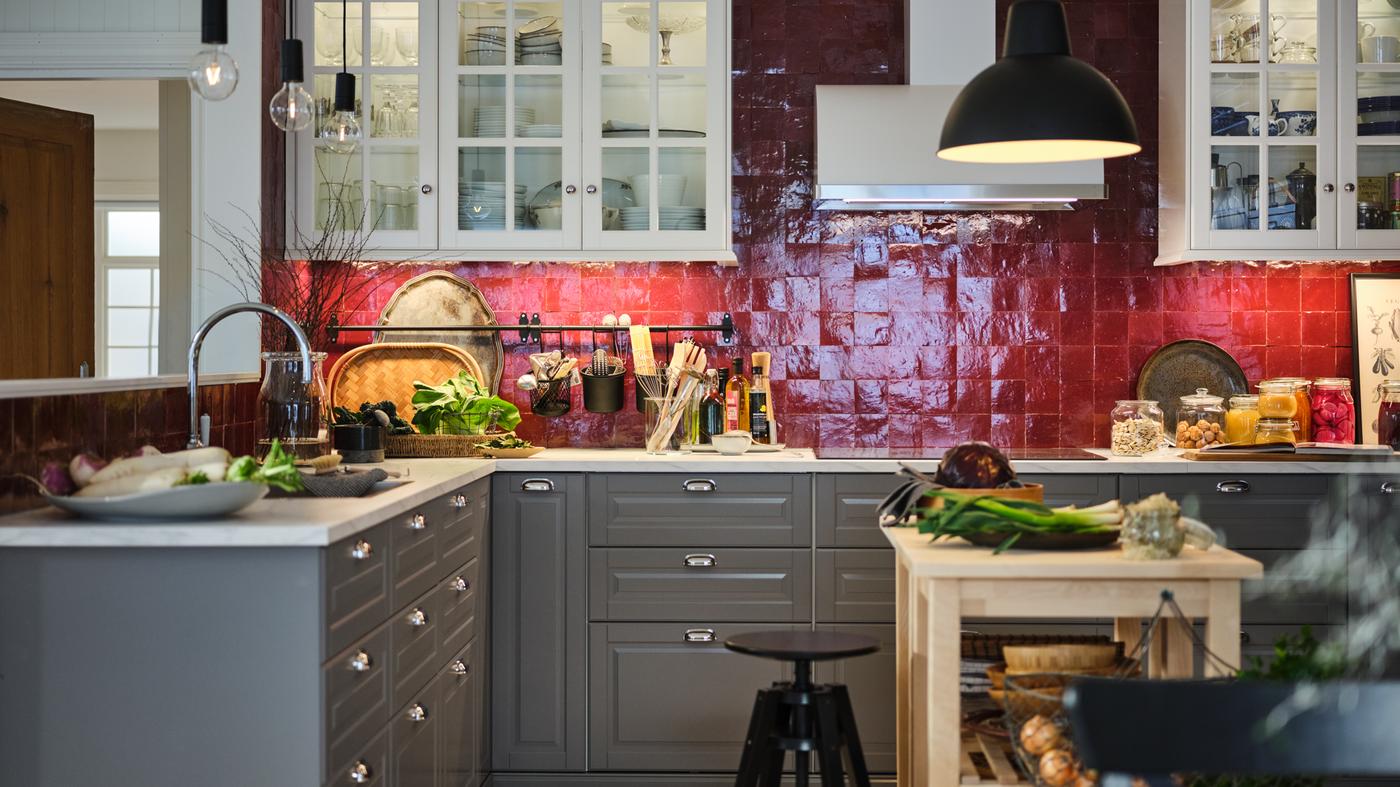 Produtos agrícolas e utensílios numa cozinha com azulejos vermelhos com armários de parede em branco, uma bancada com efeito mármore branco e armários baixos em cinzento.