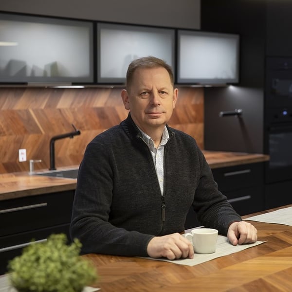 Professional man sitting at a modern office kitchen counter with a cup of coffee, wooden herringbone backsplash in the background.