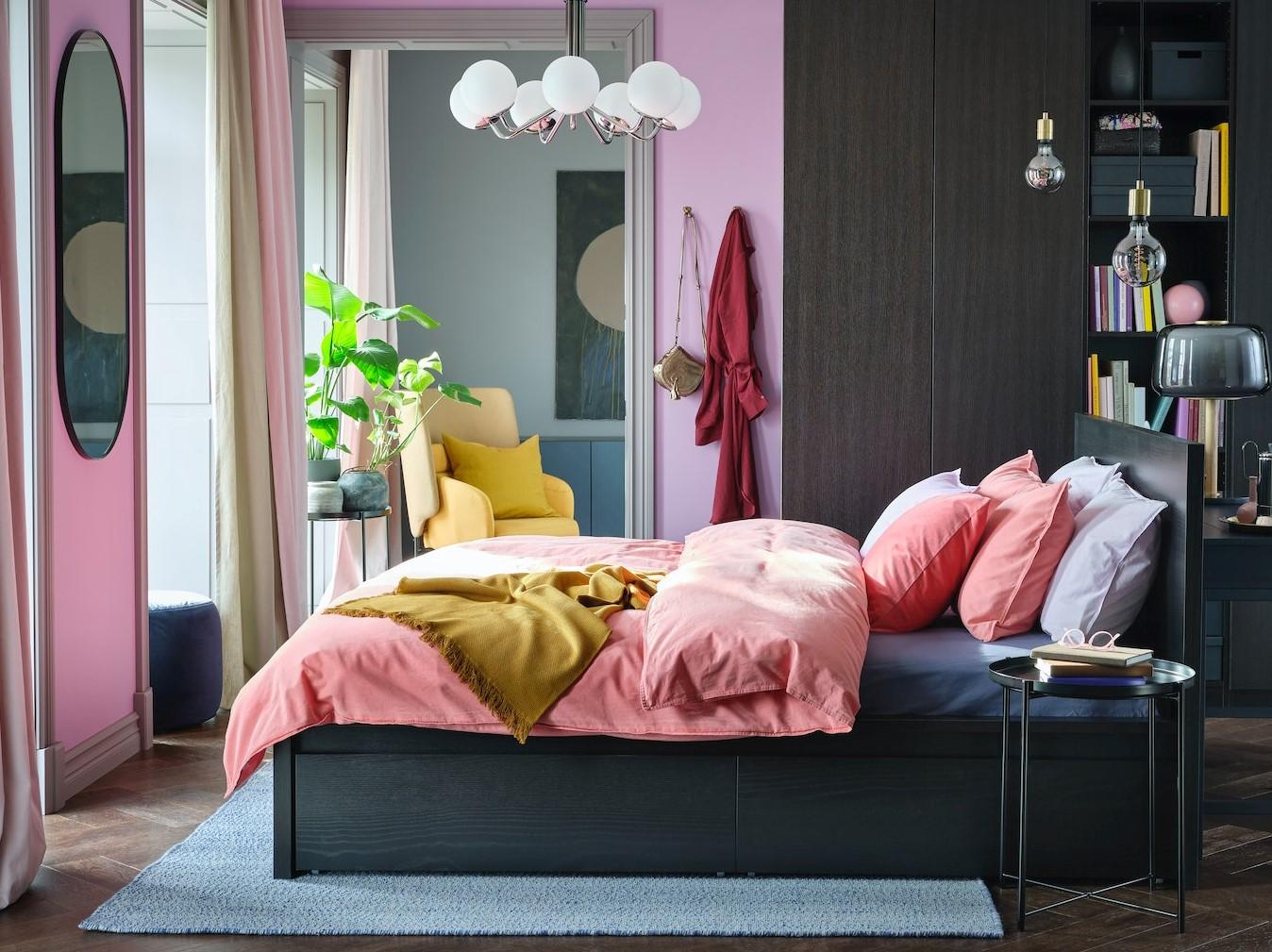 Prosluněná ložnice s černohnědou postelí MALM, barevným povlečením a velkou šatní skříní PAX/FORSAND stojící u zdi.