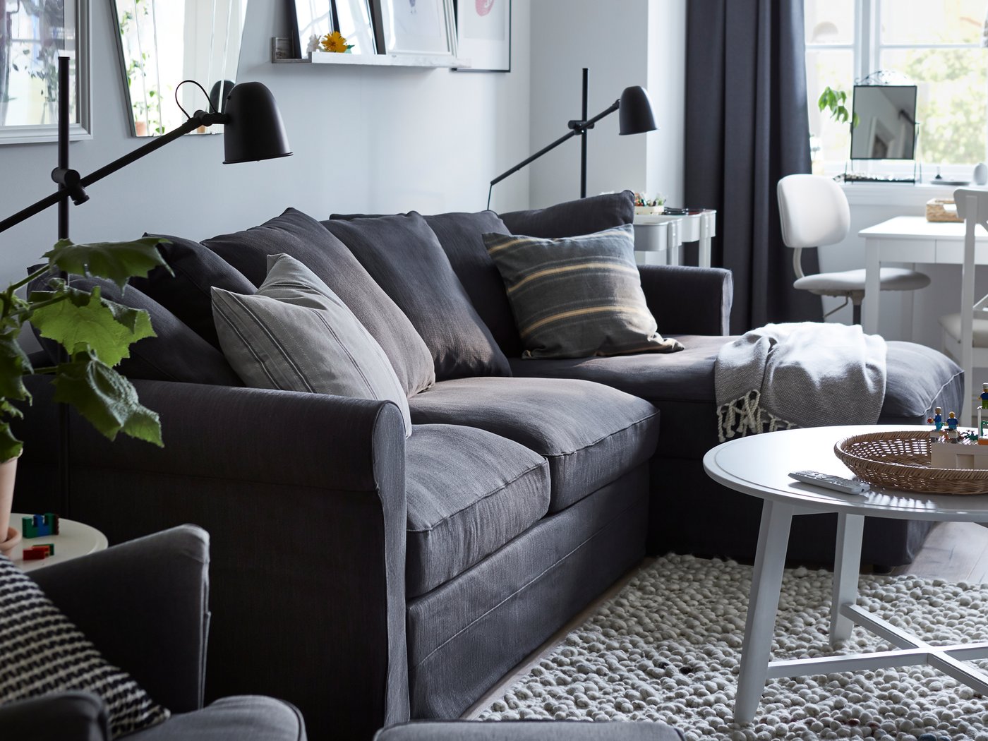 Prostorija s GRÖNLID sofa ležajem i s lenjivcem, dve SKURUP podne/čitaće crne lampe i različitim slikama na zidu.