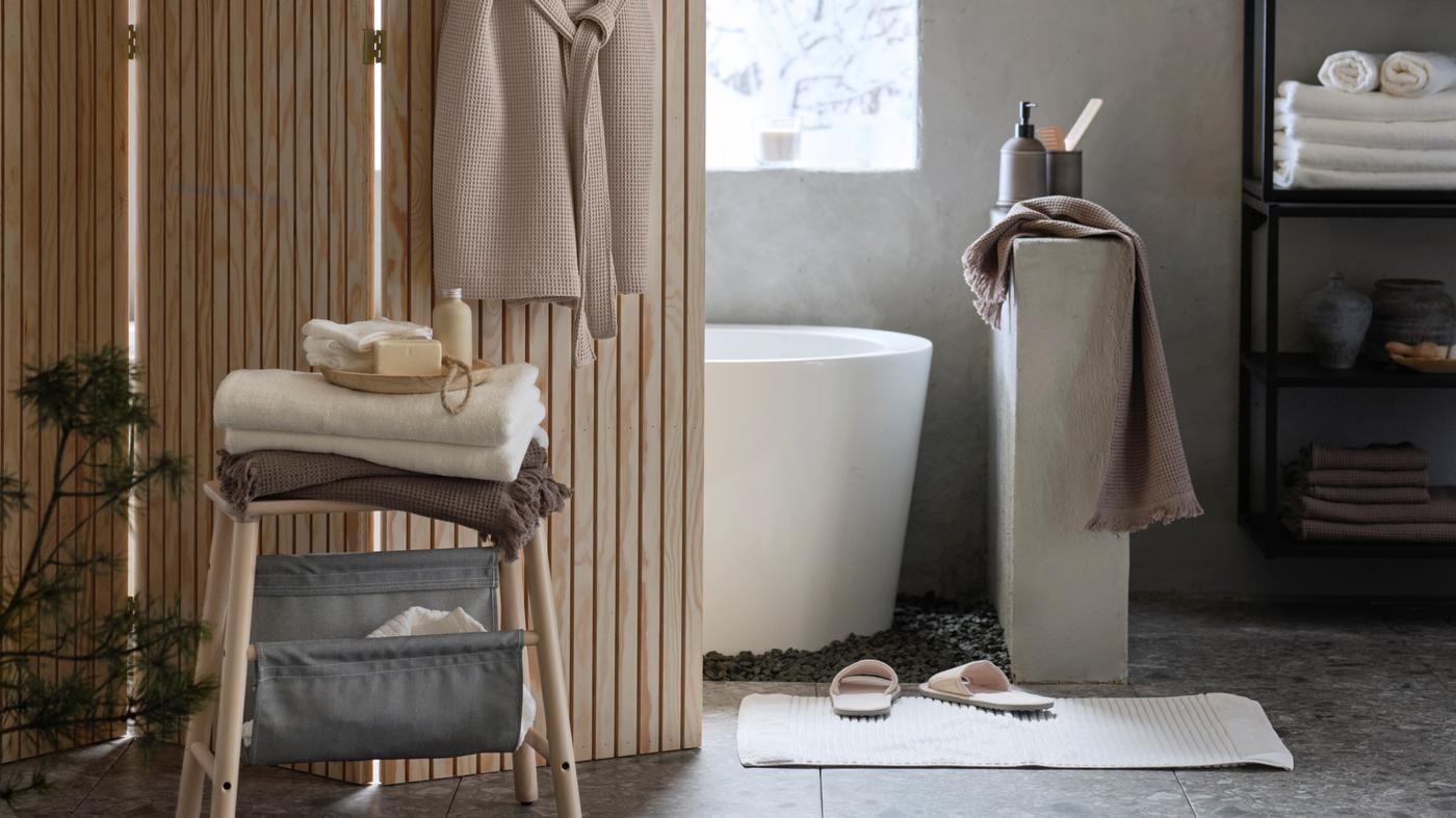 Prostorná koupelna s vanou, kterou částečně zakrývá paraván s béžovým županem pověšeným na něm.