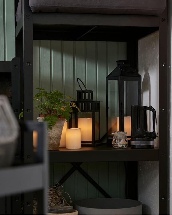 Prostredná časť policového dielu v rohu miestnosti s policami s rôznymi sviečkami LED a rastlinou.