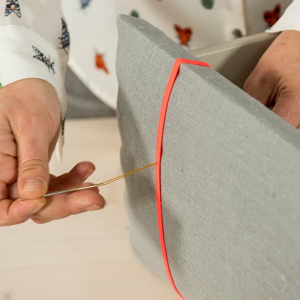 Provlékněte kousek šicí nitě pevnou jehlou a prostrčte ji zevnitř ven otvorem v čele zásuvky.