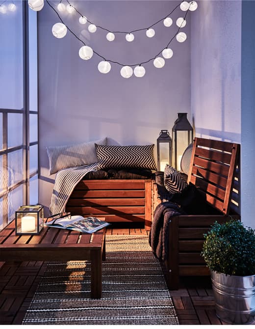 Przytulny kącik na balkonie udekorowany tekstyliami i łańcuchem świetlnym.