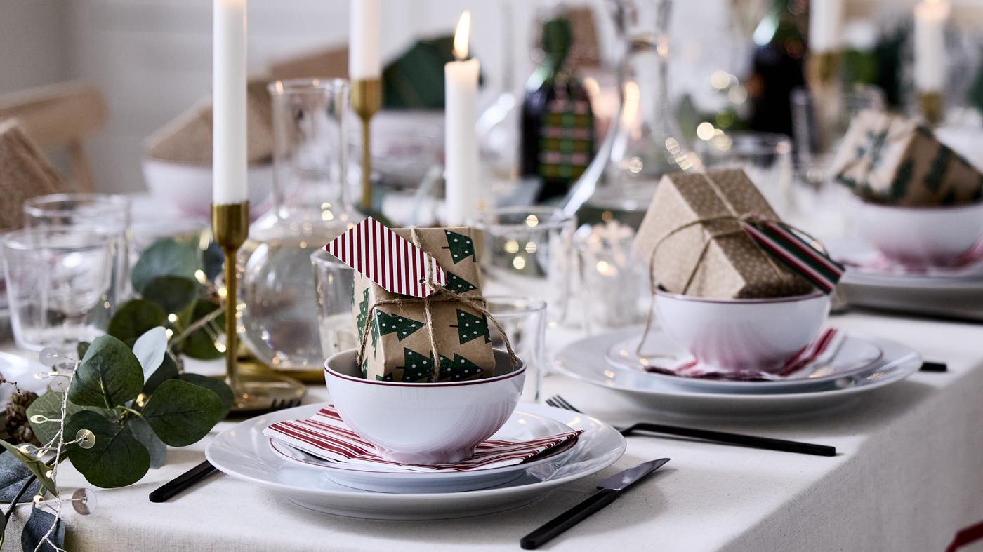 Przytulny świąteczny stół nakryty jest dekoracjami VINTERFINT, zapalonymi świecami i małymi zapakowanymi prezentami w miseczkach.