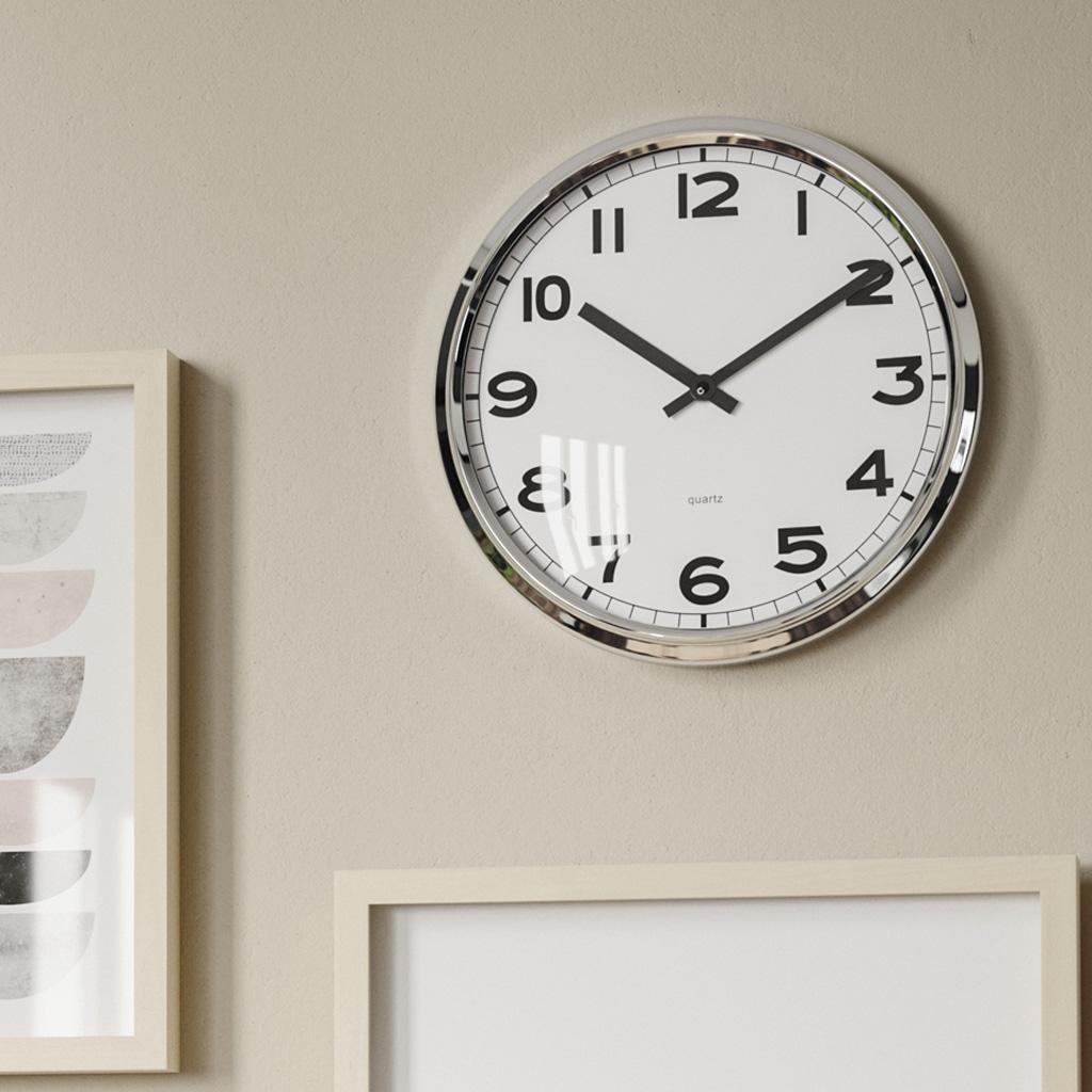 PUGG-seinäkello vaalean beigellä seinällä. Kello näyttää kymmentä yli kymmenen.