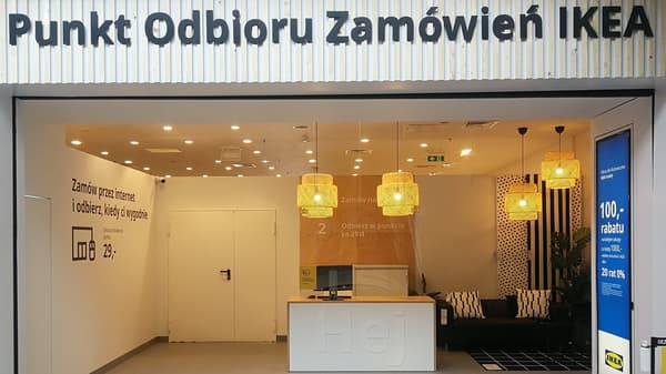 Punkt Odbioru od frontu z zewnątrz. W środku na środku stoi stanowisko z komputerem, obok kanapy.